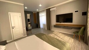 Una habitación de hotel moderna con una cama grande, un televisor de pantalla plana montado en la pared, una zona de estar con una silla y un escritorio pequeño.