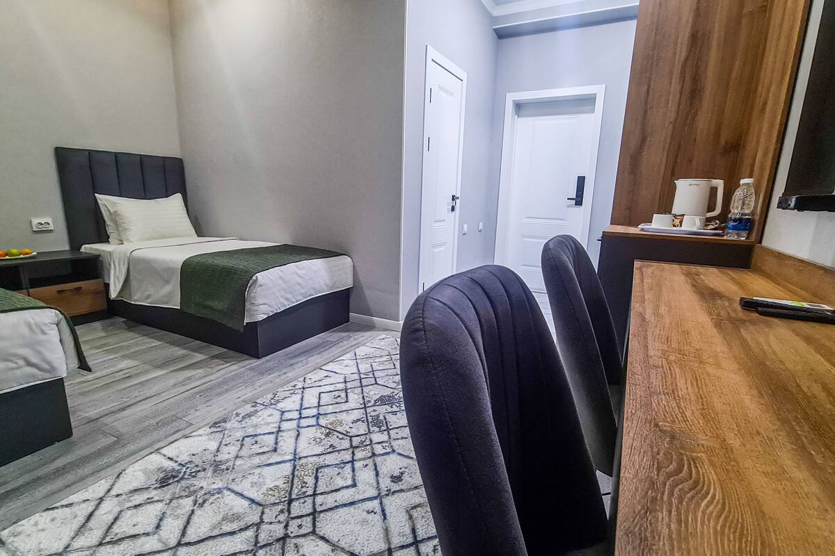 A hotel room with two beds, a wooden desk, a mirror, and a door.