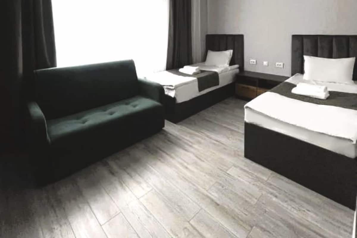 A modern hotel room with a sofa, two beds, and a large window with curtains.