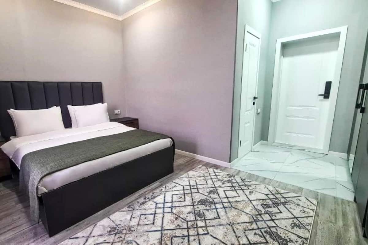 A bedroom with a bed, nightstands, a door, and a patterned rug.