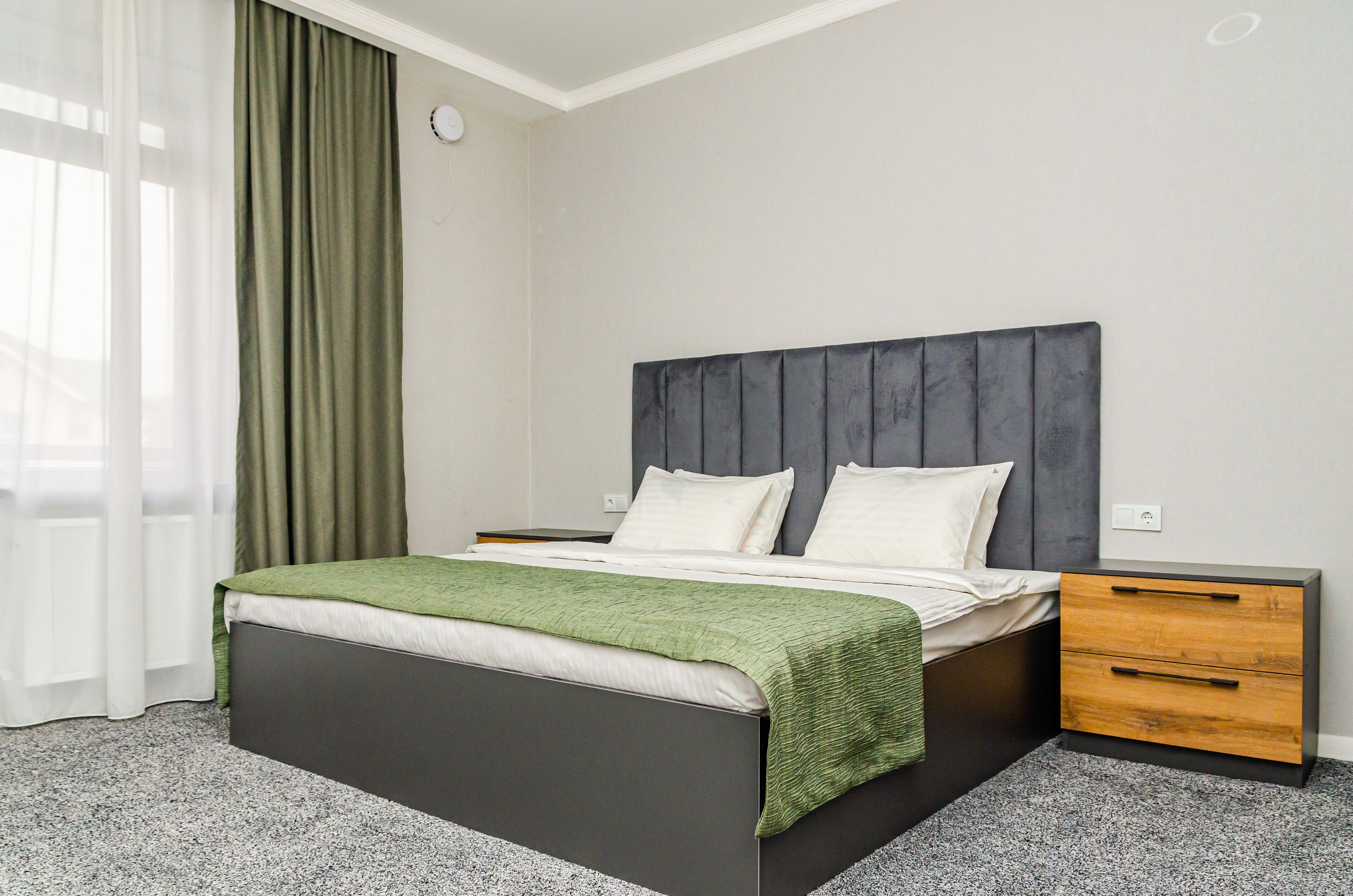 Un dormitorio moderno con cama, mesitas de noche y una cortina verde.