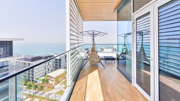 Un balcon doté d’un plancher en bois, de rampes en verre et d’un fauteuil suspendu.