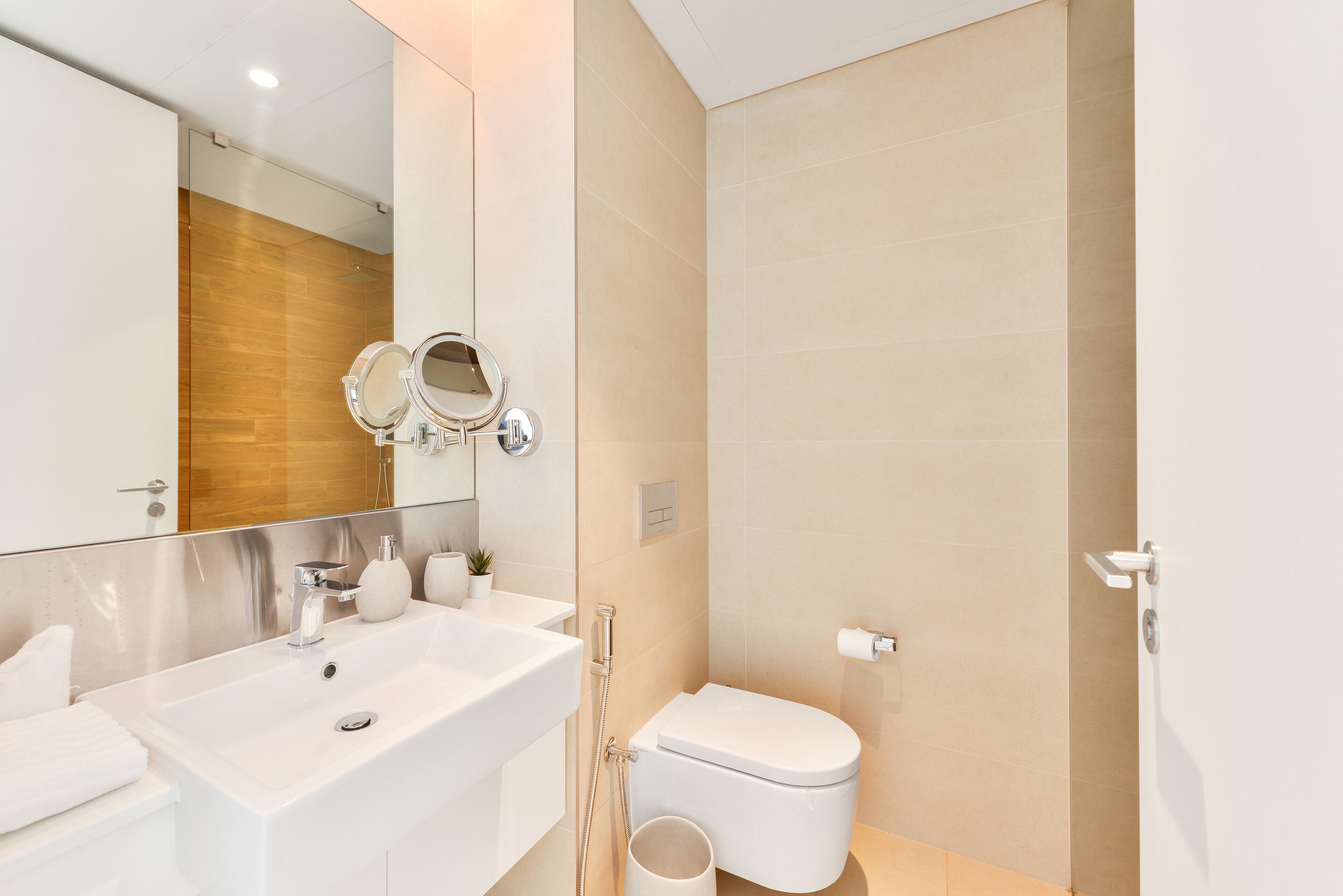 A modern bathroom with a large mirror, a white sink, a toilet, and a shower.