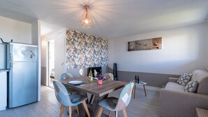 Une cuisine moderne dotée d’un réfrigérateur encastré, un coin repas avec une table et des chaises en bois, et un salon avec un canapé et une table basse.