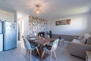 Una cocina moderna con refrigerador empotrado, un comedor con mesa y sillas de madera, y una sala de estar con sofá y mesa de centro.