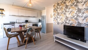 Une cuisine moderne avec des meubles blancs, une table à manger en bois et un téléviseur à écran plat posé sur un meuble blanc.