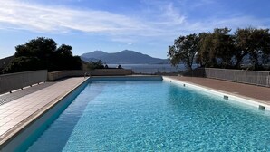 Une piscine rectangulaire à l’eau d’un bleu limpide, entourée d’une terrasse carrelée et d’une rambarde en métal. Au fond, on aperçoit des arbres et une chaîne de montagnes.