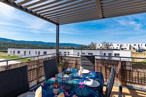 Un balcon avec une table dressée pour le dîner, offrant une vue sur un paysage montagneux et un bâtiment moderne.