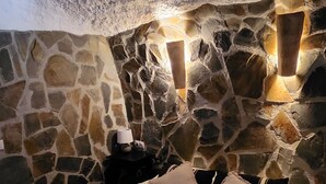 Un dormitorio con paredes de piedra, una cama, almohadas y una mesita de noche.