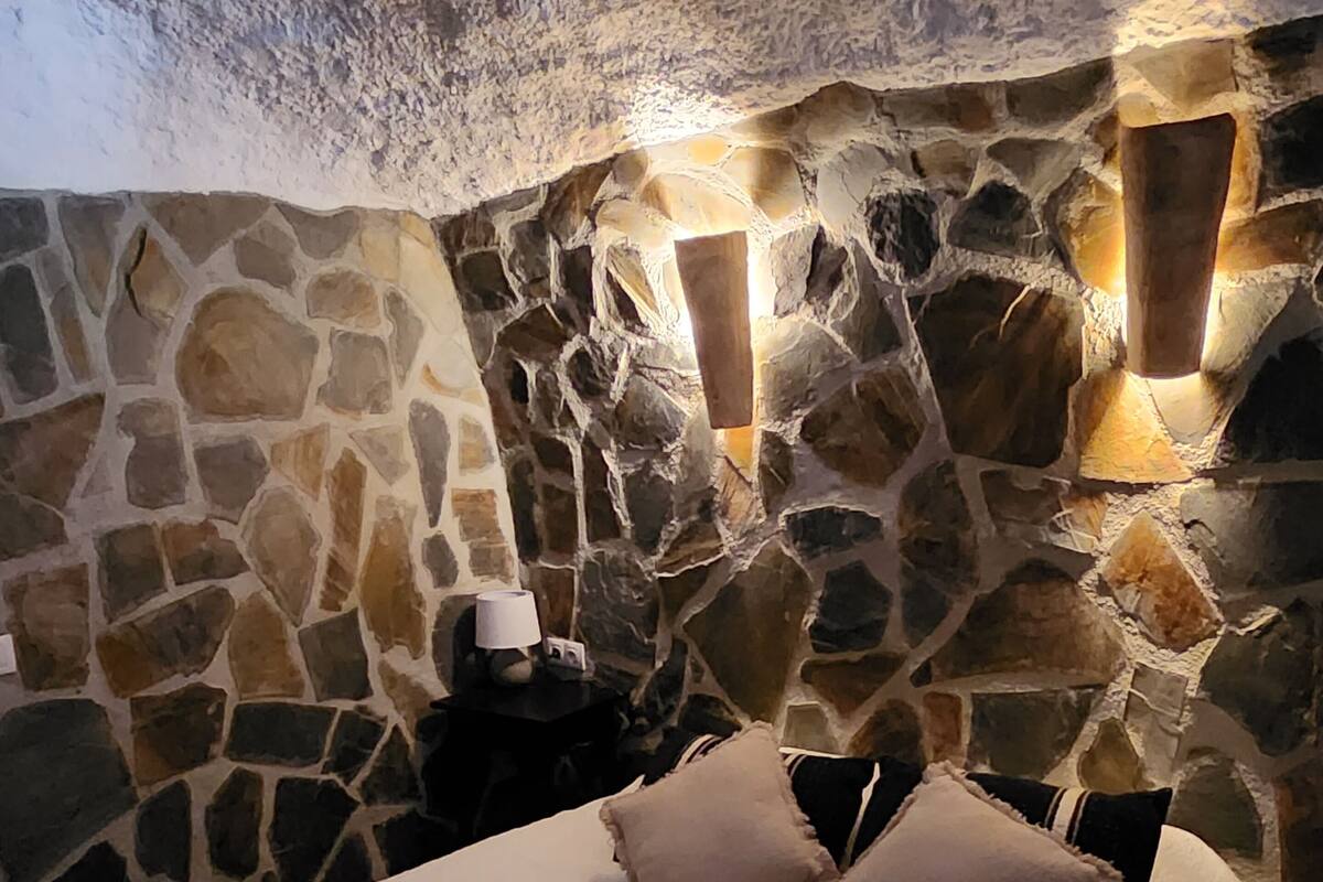 Un dormitorio con paredes de piedra, una cama, almohadas y una mesita de noche.