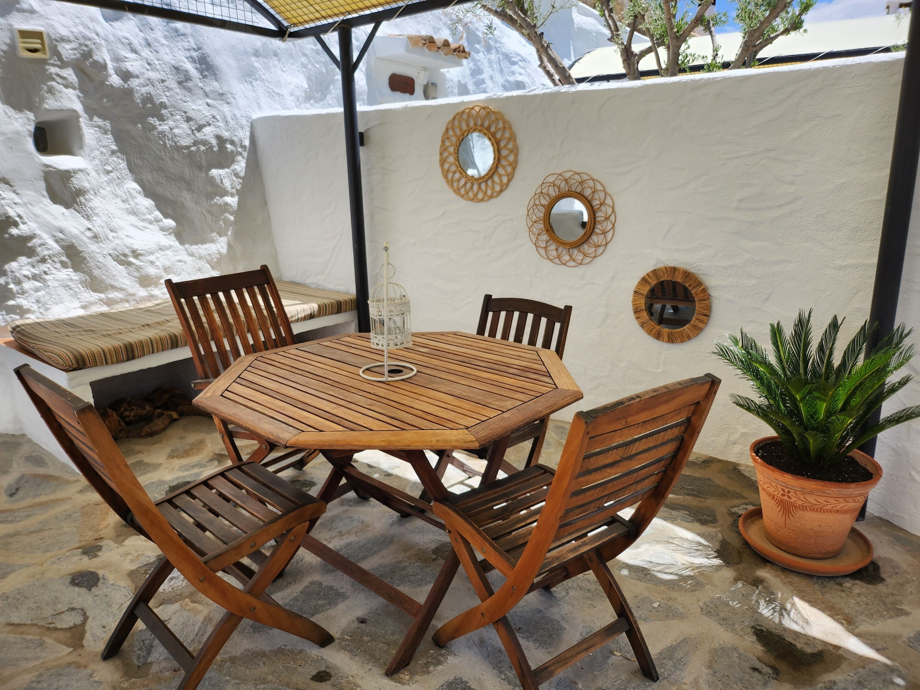 A wooden table and chairs set outdoors with a white wall and decorative mirrors.