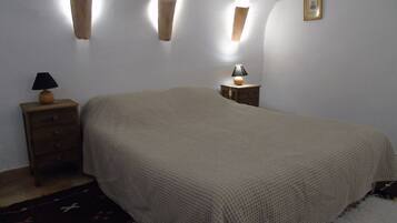 A bedroom with a bed, a nightstand with a lamp, and wall-mounted sconces.