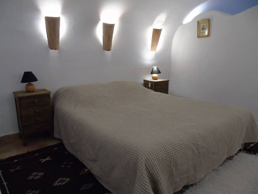 A bedroom with a bed, a nightstand with a lamp, and wall-mounted sconces.