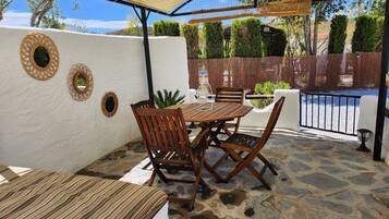 Un patio con una mesa y sillas de madera redonda, un área cubierta con un toldo amarillo y un suelo de piedra.