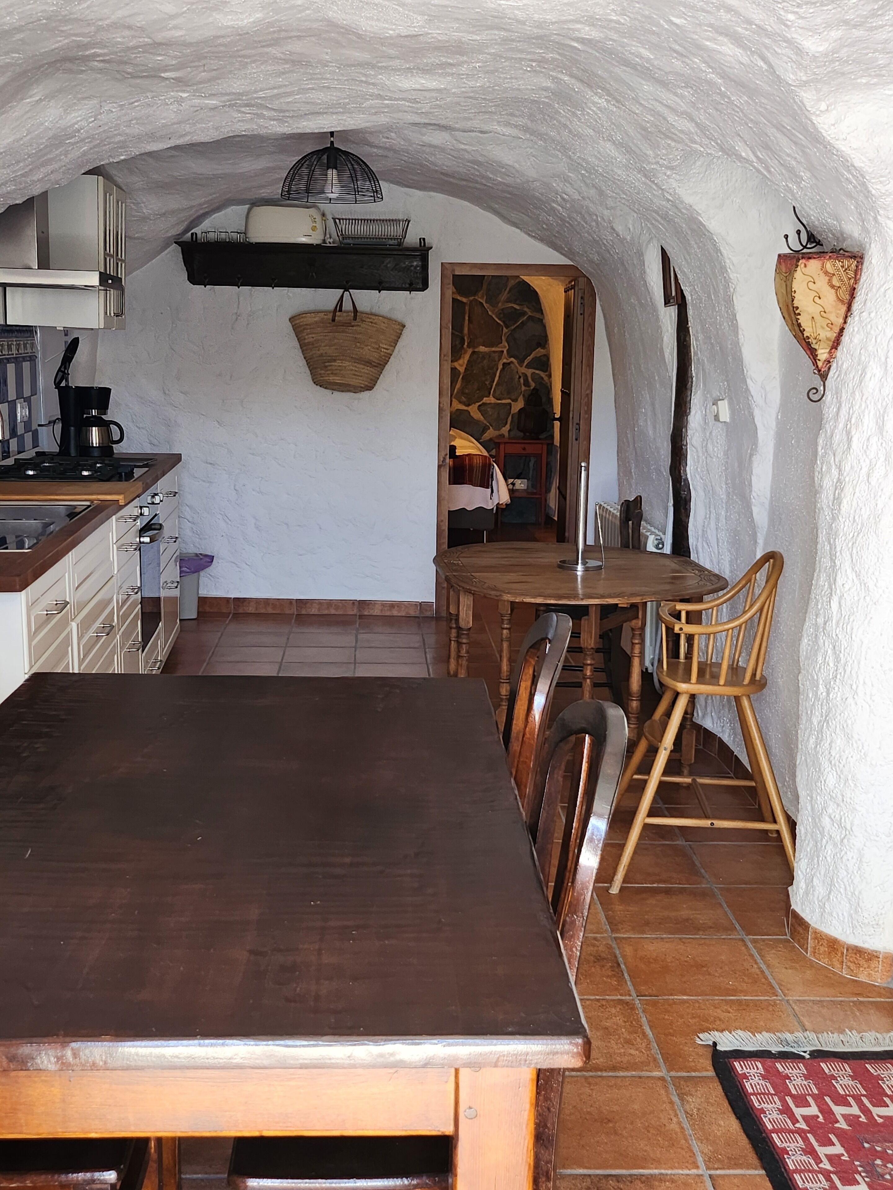 A spacious kitchen with a large wooden table, a stove, and a hanging light fixture.
