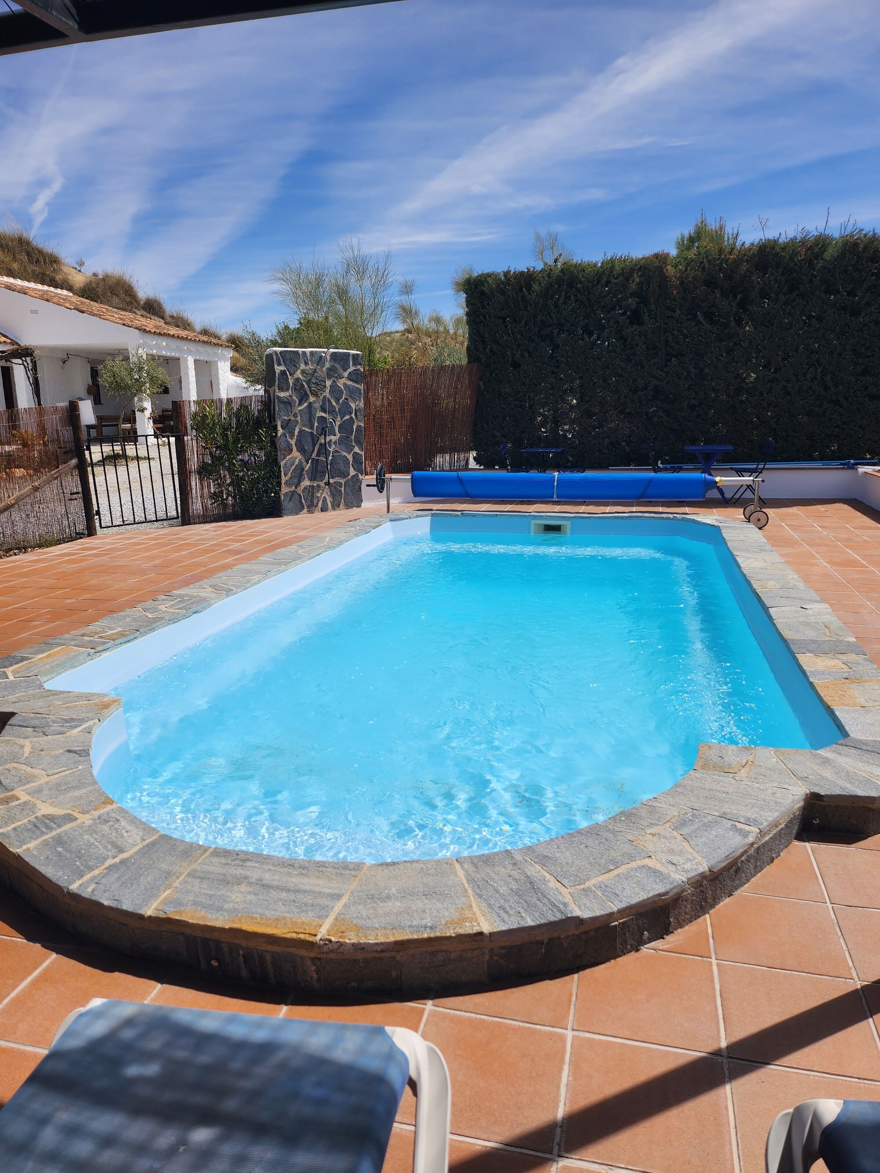 Une piscine rectangulaire bordée de pierres, avec un muret en pierre et un toboggan bleu.