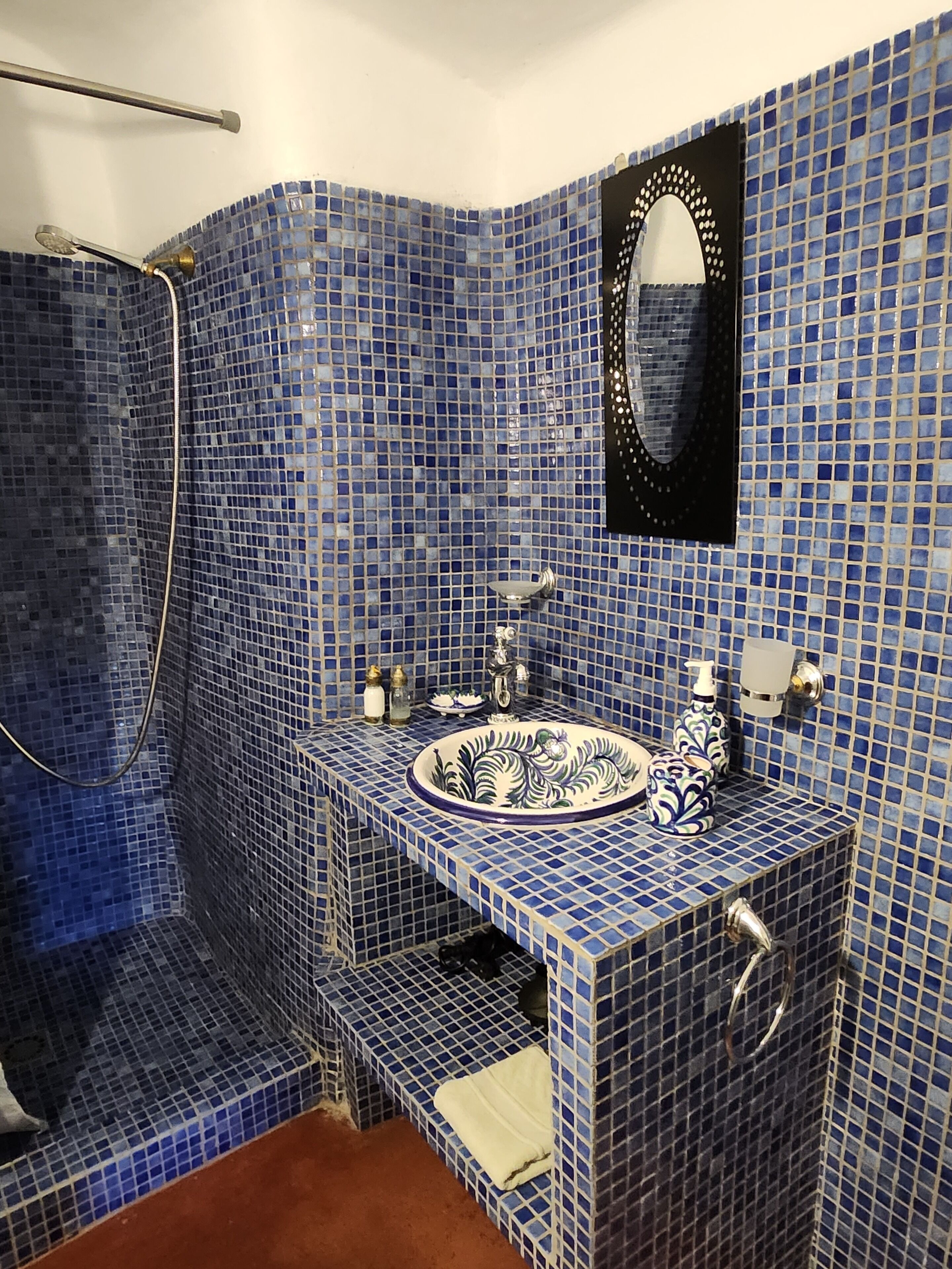 A bathroom with blue mosaic tiles, a sink with a decorative basin, a mirror, and a shower area.