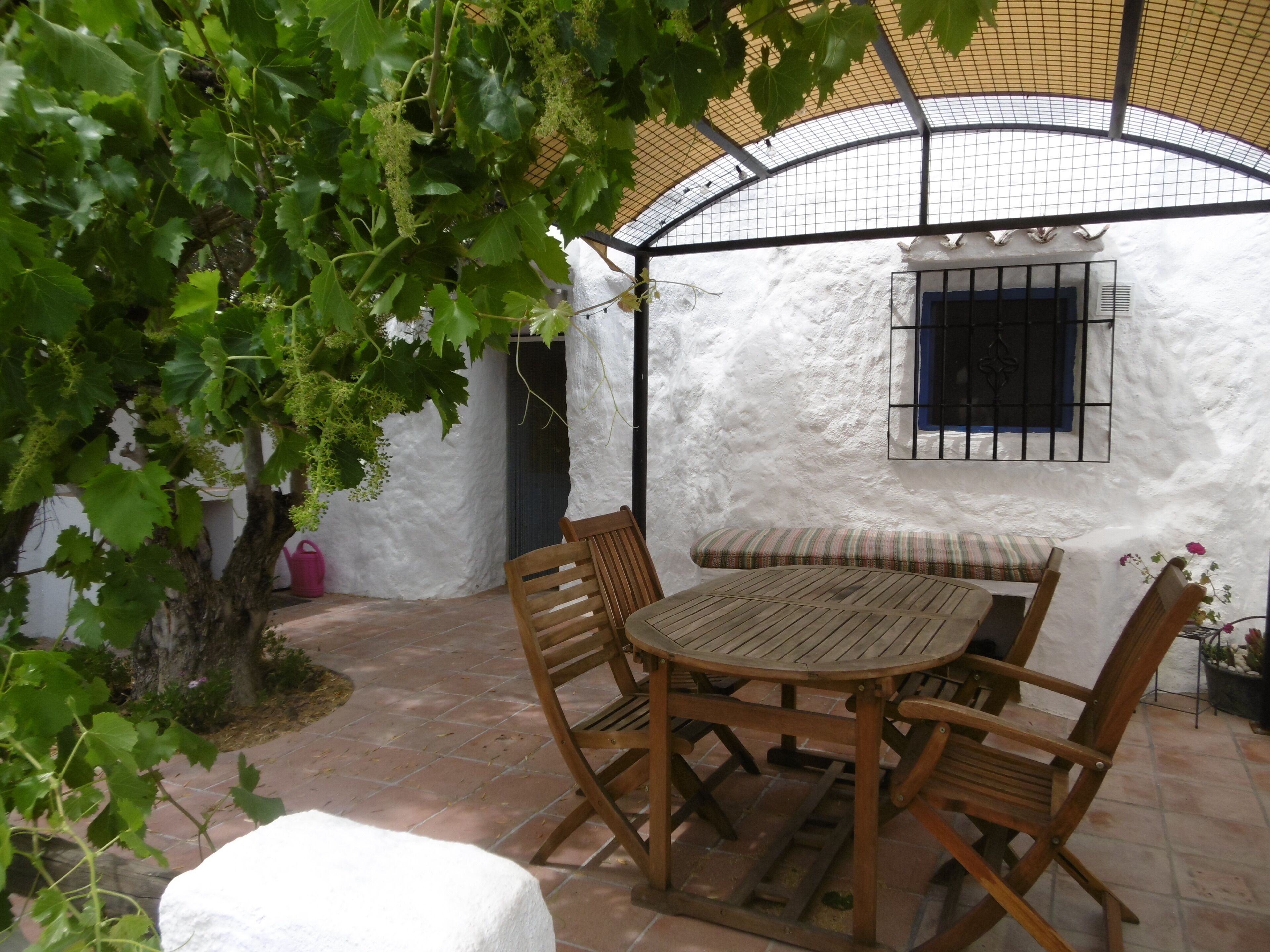 A patio with a round wooden table and chairs, surrounded by white walls and a covered area with a curved roof.