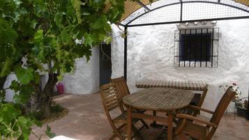 A patio with a round wooden table and chairs, surrounded by white walls and a covered area with a curved roof.
