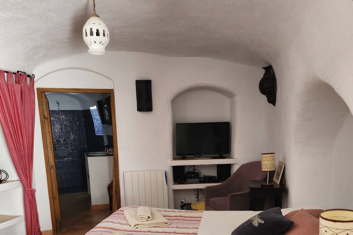Un dormitorio con cama, televisión, lámpara y baño visible a través de una puerta abierta.