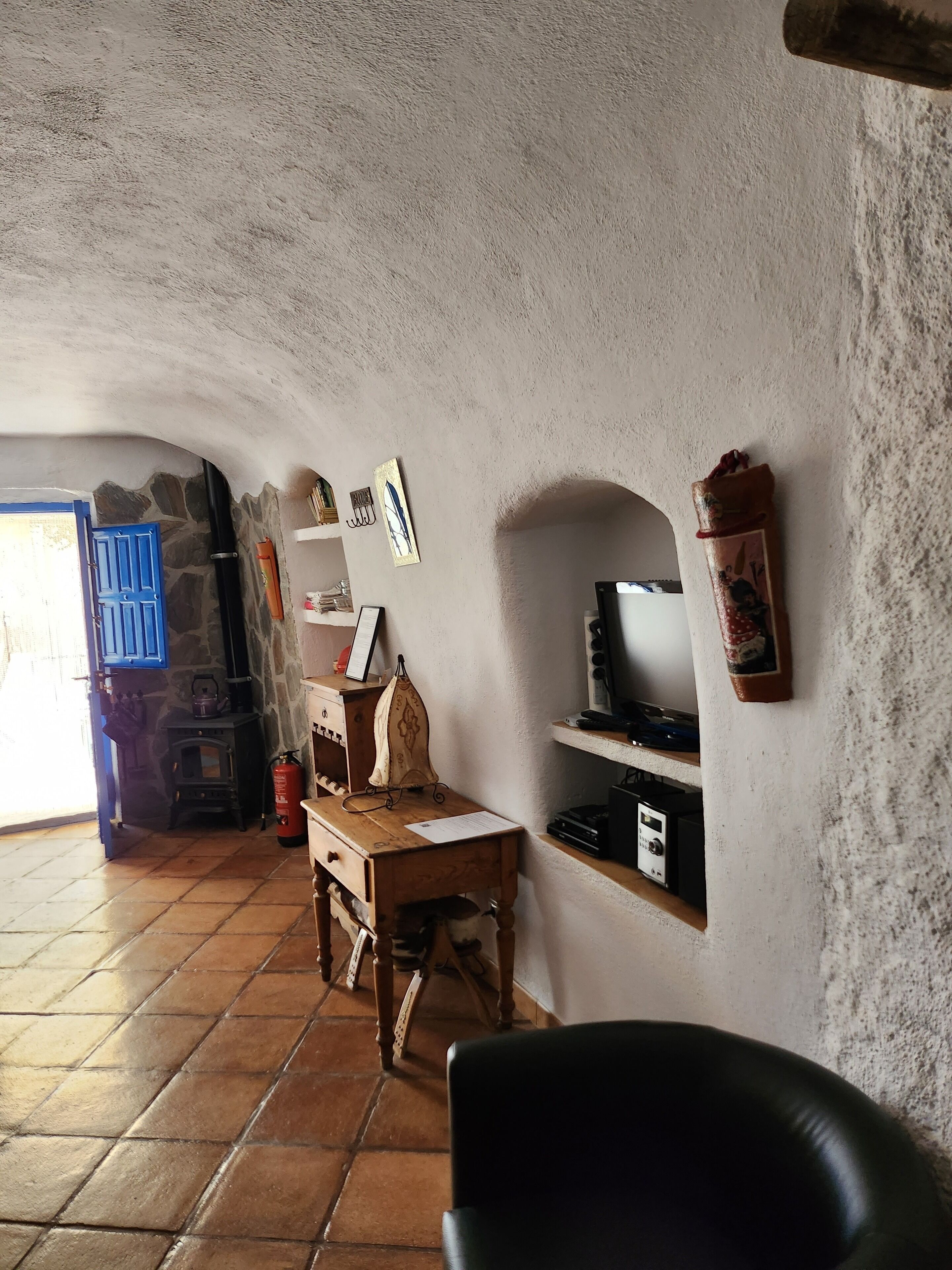 Ein rustikales Interieur mit Steinwand, Holztisch, schwarzem Stuhl, blauer Tür und kleinem Kamin.