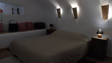 A dimly lit bedroom with a large bed, a nightstand with a lamp, and wall-mounted sconces.