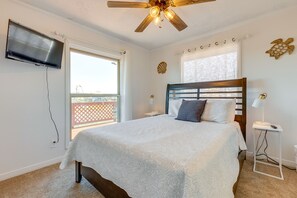 A bedroom with a bed, a ceiling fan, a TV mounted on the wall, and a window with a view of a balcony. - Breezy Dauphin Island Vacation Rental with Deck! (Dauphin Island)
