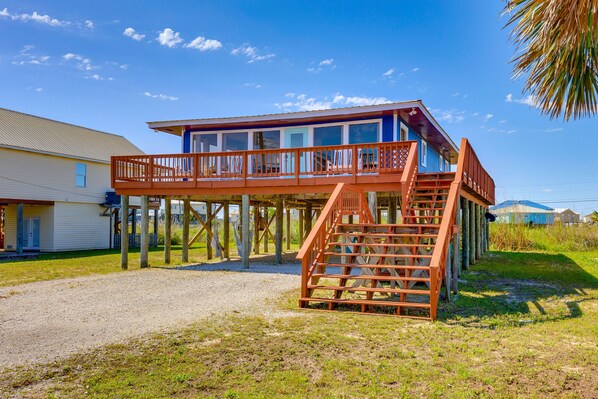 A two-story house with a wooden deck and a staircase leading to the upper floor. - Breezy Dauphin Island Vacation Rental with Deck! (Dauphin Island)