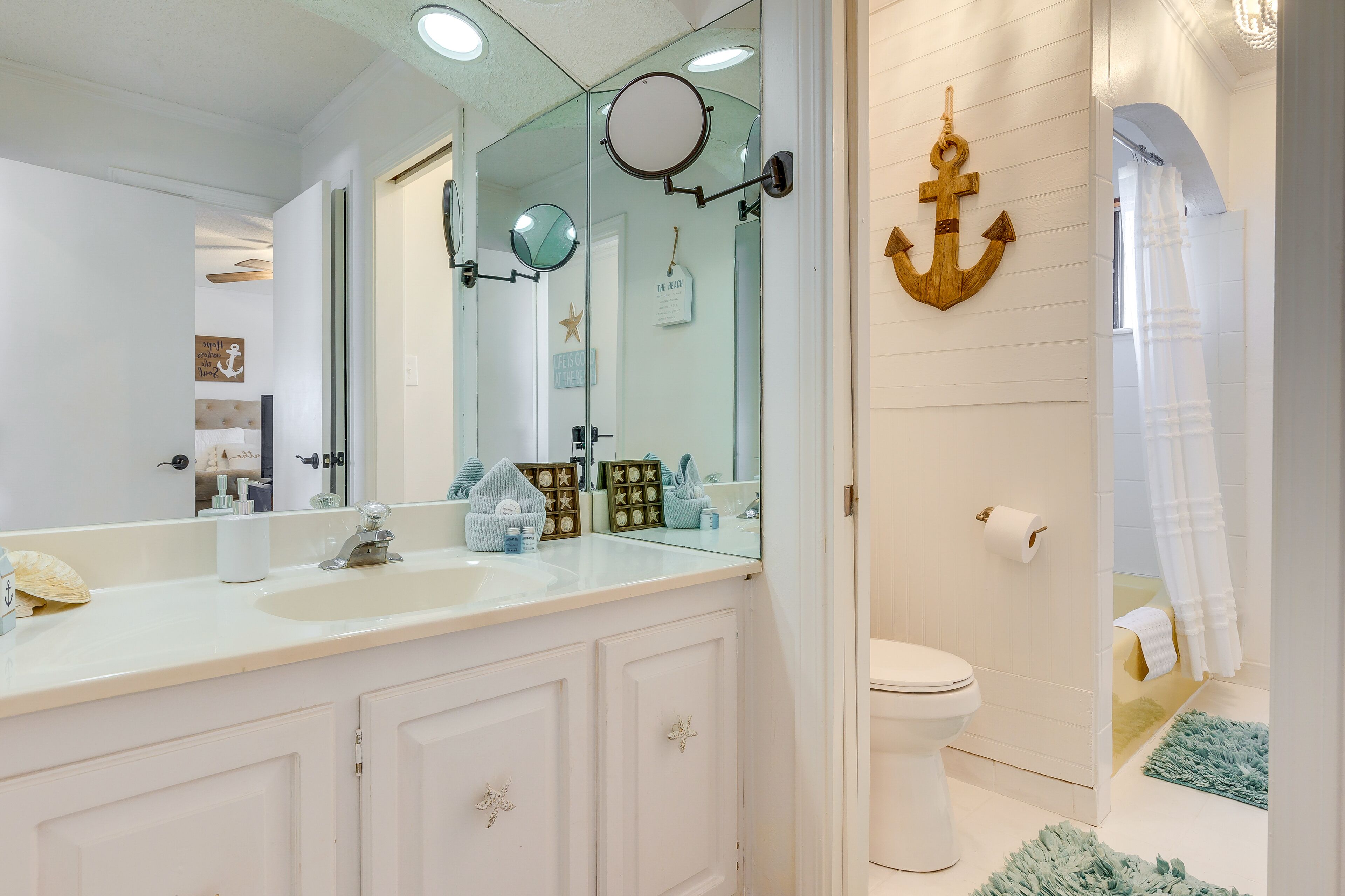 Une salle de bain avec un meuble-lavabo blanc, un grand miroir et un élément décoratif en forme d’ancre en bois.