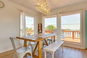 A dining area with a wooden table, white chairs, a bench, and a chandelier. - Breezy Dauphin Island Vacation Rental with Deck! (Dauphin Island)