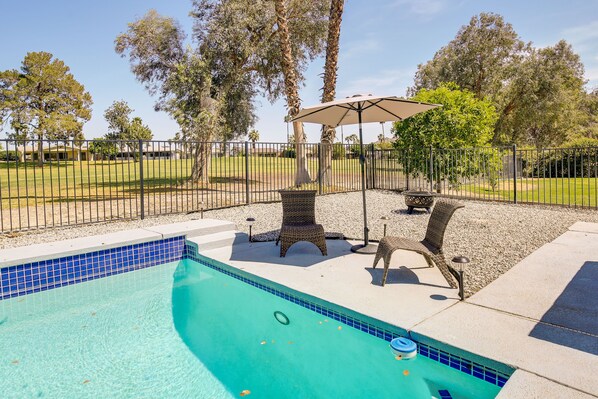 A swimming pool with a tiled edge, surrounded by a fence, and shaded by a canopy.