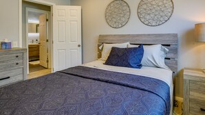 A bedroom with a bed, a nightstand, a dresser, and a door leading to a bathroom. - Pool & Spa: Palm Desert Home Near Golf! (Palm Desert)