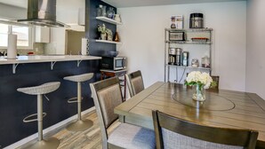 A modern kitchen with a dining area, featuring a large island, bar stools, and a vase with flowers on the table. - Pool & Spa: Palm Desert Home Near Golf! (Palm Desert)