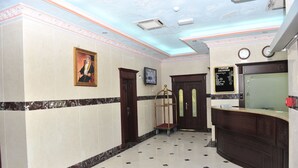 A hotel lobby with a marble floor, a reception desk, a framed portrait, and a wall-mounted clock. - Manam Sohar Hotel Apartments (Sohar)