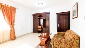 A living room with a sofa, a wooden coffee table, a patterned rug, a door, and a cabinet. - Manam Sohar Hotel Apartments (Sohar)