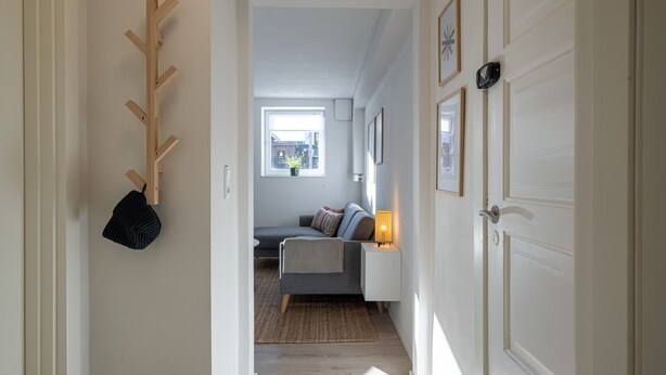 Un couloir menant à une chambre à coucher équipée d’un lit, d’une table de chevet, d’une lampe et d’un porte-manteau.