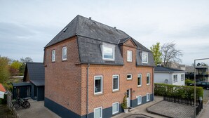 Une maison à deux étages, construite en briques, avec un toit foncé, un petit garage attenant et une allée pavée.