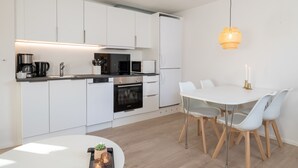 Une cuisine moderne avec des meubles blancs, un four noir et un coin repas comprenant une table et des chaises blanches.
