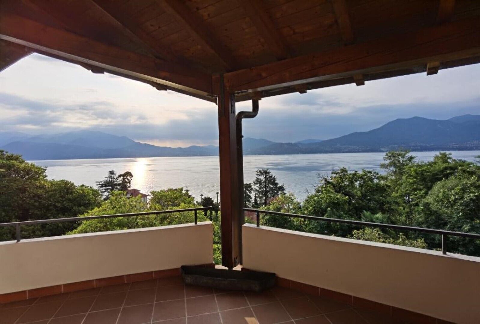 A covered balcony with a view of a lake and mountains.