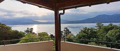 A covered balcony with a view of a lake and mountains.