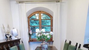 Ein Esszimmer mit einem Holztisch und sechs grünen, gepolsterten Stühlen. Auf dem Tisch steht eine Vase mit weißen Blumen.