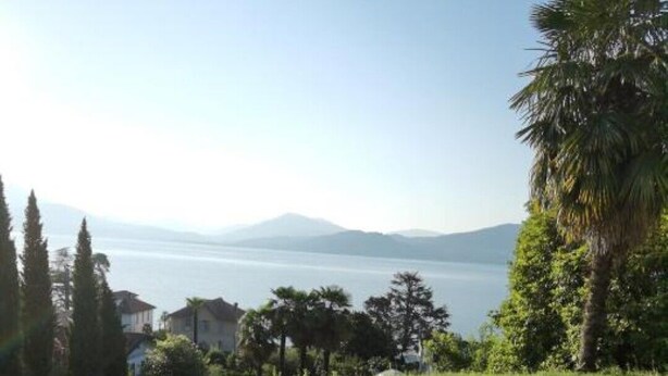Two white lounge chairs with beige cushions on a grassy lawn overlooking a body of water and distant mountains. - Villa Schaake Lago Maggiore 100m vom Strand (Gonte)