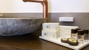 A bathroom with a stone sink, a copper faucet, and a tray with toiletries. - Liferooms b&b (Ischia)