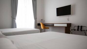 Una camera d'albergo con due letti, una scrivania, una sedia e una televisione appesa al muro.