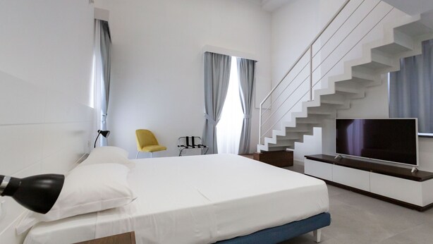 A modern bedroom with a large bed, a TV, a chair, and a staircase. - Liferooms b&b (Ischia)