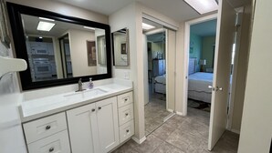 Une salle de bain moderne avec un grand miroir, des meubles blancs et un sol carrelé.