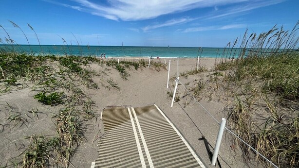 Un sentier bordant la plage, menant à l’océan, avec un ciel dégagé.
