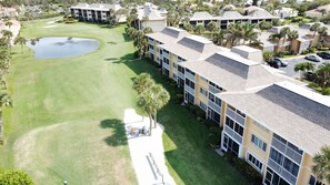 A golf course with a pond, surrounded by multi-story buildings with balconies and a parking area. - Beach Paradise! Relaxation, Sports, Beach, all in the Village! (Fort Pierce)