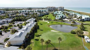 Un parcours de golf avec un étang, entouré de bâtiments d’hôtel et de palmiers.