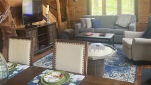 A cozy cabin-style room with a wooden interior, a sofa, a dining table, and a television. - Tanzanite-- The "GEM" with a Hot Tub & WiFi!! (Slade)